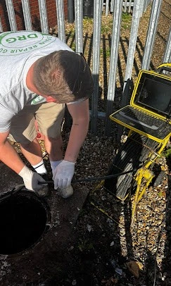 Drain engineer working at an open manhole with CCTV inspection equipment beside the access point.