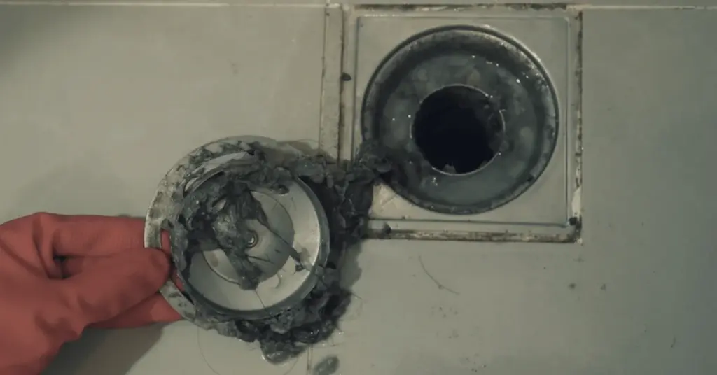 Hand removing hair and debris from a drain opening during drain cleaning.
